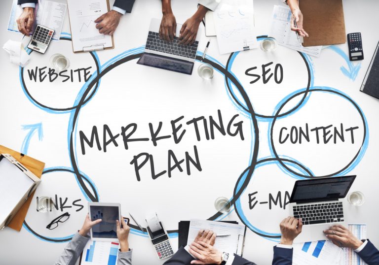 marketing plan diagram written on a desk with employees working around it