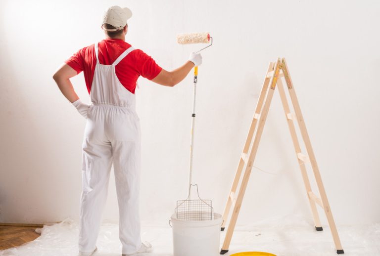 a man painting a wall white with a ladder and roller