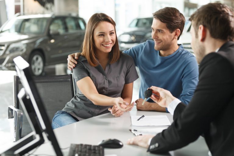 male car dealer offering car keys to a young couple in the dealership